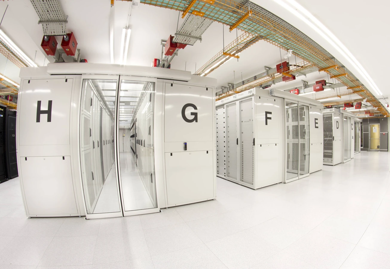 Radore Veri Merkezi'nin gerçek server salonunda, H–G–F gibi etiketli kabinler ve koridorun farklı açıdan görünümü.